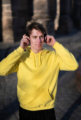 Smiling man in yellow sweatshirt with a headphones listening music outdoors