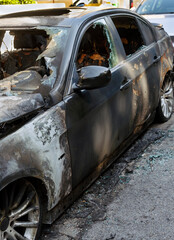 Vertical photo of burnt car. Setting fire to cars, terrorist attack, Vandalism, mafia. Remains of a burned out car on roadside down in the middle of the street. Windows shatter from the explosion