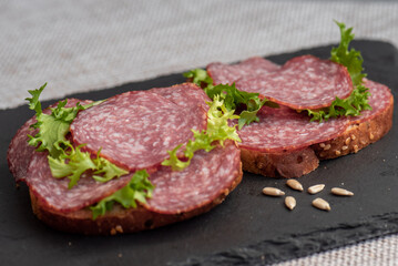 sliced ​​salami and lettuce on black background, top view. open sandwiches with sliced ​​salami sausage on rye bread