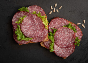 sliced ​​salami and lettuce on black background, top view. open sandwiches with sliced ​​salami sausage on rye bread