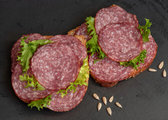 sliced ​​salami and lettuce on black background, top view. open sandwiches with sliced ​​salami sausage on rye bread