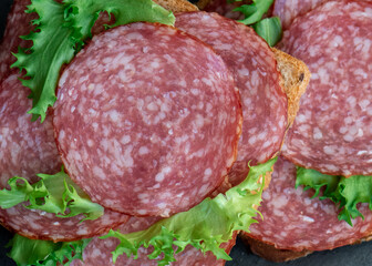 sliced ​​salami and lettuce on black background, top view. open sandwiches with sliced ​​salami sausage on rye bread
