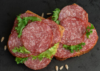 sliced ​​salami and lettuce on black background, top view. open sandwiches with sliced ​​salami sausage on rye bread