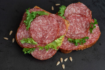 sliced ​​salami and lettuce on black background, top view. open sandwiches with sliced ​​salami sausage on rye bread