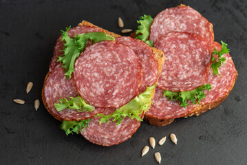 sliced ​​salami and lettuce on black background, top view. open sandwiches with sliced ​​salami sausage on rye bread