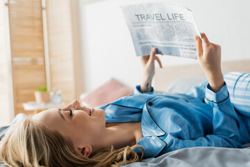 Obraz premium happy young woman smiling while reading travel life newspaper in bed.