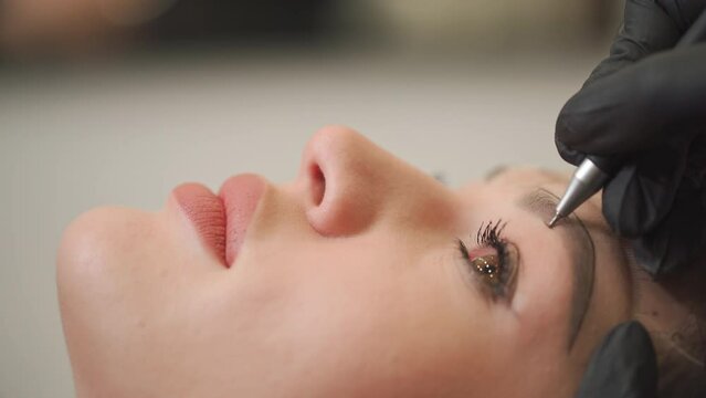 A woman master makes permanent eyebrow makeup to a young beautiful girl in a beauty salon.Microblading, eyebrow tattoo in a beauty salon.
