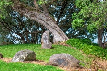 Carved stone statue on the grassy lawn in front of a Pohutukawa tree