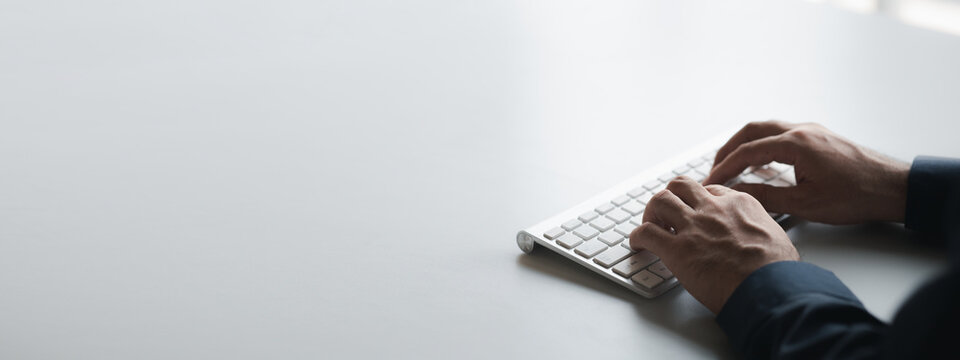 Person typing on a computer keyboard, businessman is working in a startup company's office, he is typing messages to his colleagues and making financial documents summarizing the meetings. Copy space.