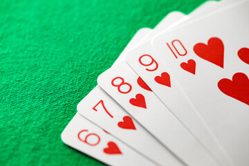 Playing cards, poker combination straight flush red suit of hearts from six to ten, on green background, selective focus
