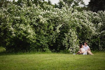 Young man and woman couple in a blooming garden near jasmine bush. Tender holding each other. Spring lovestory. Brown-haired girl with long hairs with her boyfriend or husband. Young couple on a date