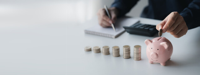 A businessman holding a coin in a piggy bank. Placing coins in a row from low to high is comparable to saving money to grow more. The concept of growing savings and saving by investing in stock funds.