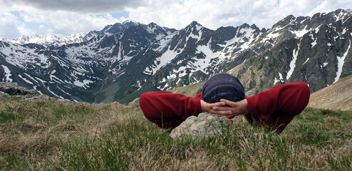 Back view of a solo traveler in the Kaçkar Mountains. The man watches the mountain peaks and valley while lying down and resting.