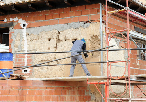 Alba&ntilde;il picando con la piocha un viejo muro de adobe para la reconstrucci&oacute;n de la nueva casa. Trabajador de la construcci&oacute;n en el andamio utilizando la piqueta. 