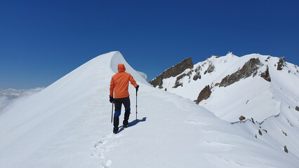 A male climber with a hiking pole walks to the top of the snow-capped mountain. Erciyes Mountain east ridge route in Kayseri, Turkey