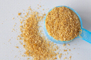 Close-up of brown pellets of bone broth in a blue spoon against a beige background. Collagen for...