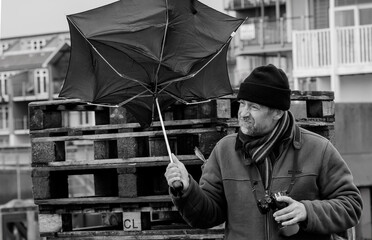 Man with an umbrella on a stormy day, battles against the wind. Captured in monochrome for dramatic...
