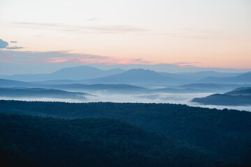 Morning fog filled the lowlands in the river valley, the mountains are visible in the distance, the taiga at dawn of the day, the bluish perspective.