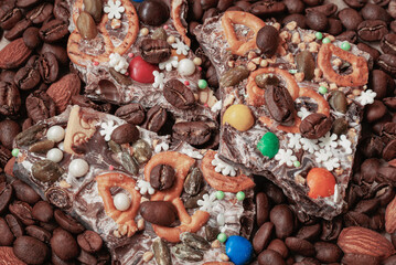 Broken pieces of handmade chocolate with a variety of additives on the background of coffee beans, almonds