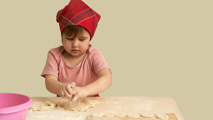 A little girl is carving cookies out of a sheet of dough with a glass. Her face is in flour and her hands are in the dough. Copy space.
