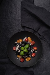 Food photography of black spaghetti with . tomatoes,basil and parmesan in a black  plate. Dark texture background. Top view..