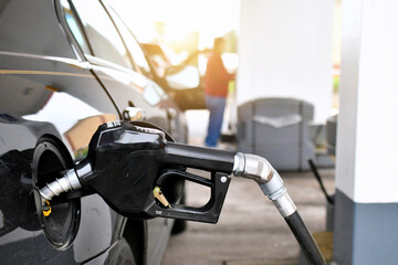 A gasoline pump handle in a gas tank of vehicle with another customer at gas pump in background