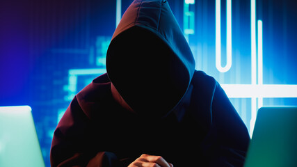 a man wearing black hoodie, sitting on the desk with laptop, with technology-themed background design, hacker man concept.
