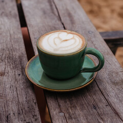 Morning cappuccino with a beautiful foam in a green mug on a wooden table. Delicious coffee on vegetable milk side view