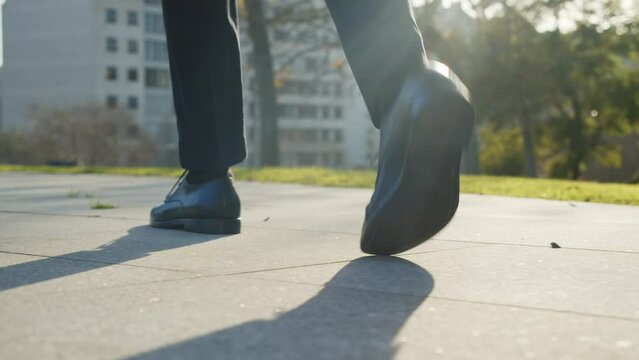 Rear close-up view to the businessman in a black new shoes walks quickly on the street. Legs of a businessman in fashionable shoes walking outdoors. Business concept. Stylish men wears. Low angle