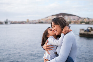 Mother and daughter embraced by the sea at sunset outdoors. Concept: Lifestyle, family care, love