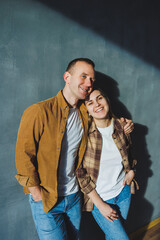 Smiling happy couple dressed in jeans and shirts standing on a gray wall background, isolated gray concrete wall background. The concept of a happy couple in love.