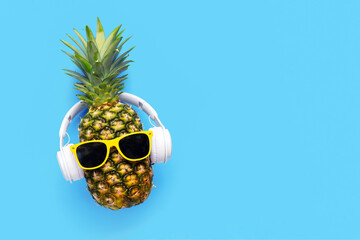 Ripe pineapple with sunglasses and headphones on blue background