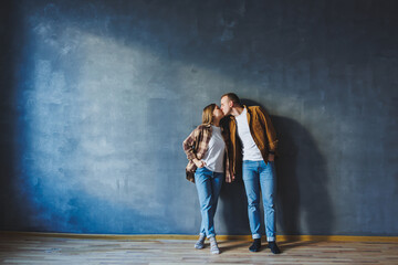 Obraz na płótnie Canvas A young married couple in love in shirts and jeans on the background of a gray wall. The concept of happy family relationships. A man and a woman are hugging