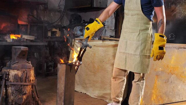 A blacksmith in a blacksmith shop dips a burning newly forged sword into a container with oil for hardening,