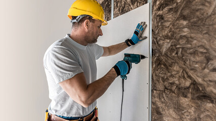 An electric quick screwdriver in the hand of a plasterer is screwing the plasterboard to the metal frame.