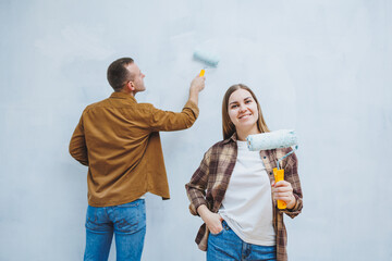 Young married couple in love in shirts and jeans doing renovations, renewing painting walls with a roller, preparing to move into a new house, selective focus