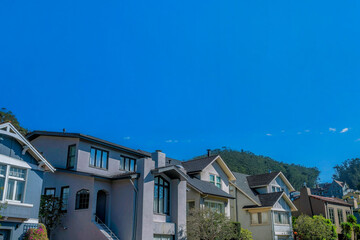 Street view of houses against blue sky in San Francisco California neighborhood. Real estate landscape with homes featuring gray walls lit by sunlight on a sunny day.