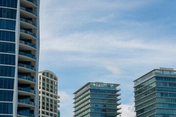 Modern high rise condominiums with glass railings on the balconies at Miami, FL. There is a white building on the left at the back along with the glass buildings against the sky background.