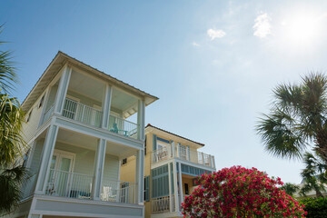 Low angle view of two houses with topiary bougainvillea at the front under the sun in Destin, FL. There is house on left with white wood sidings beside the house on right with board and batten siding.