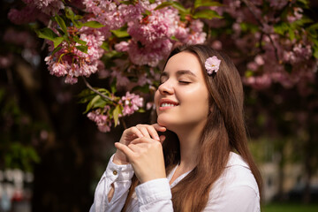 Young woman romantic close up portret in a blooming sakura garden. Wind is hairs. Spring story....