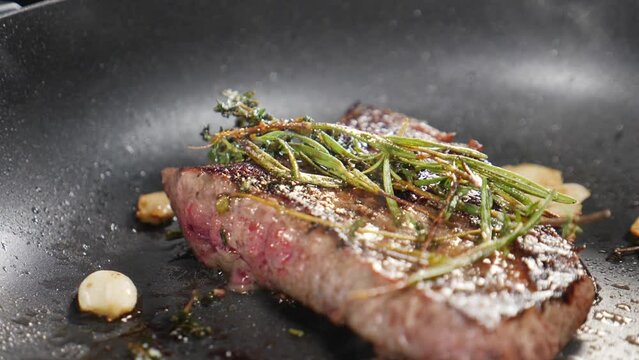 Fresh raw steak being fried with rosemary, garlic and herbs, close up. Juicy meat being prepared for serving. Cooking in restaurant. Fine cuisine. slow motion. Juicy meat being fried with white smoke