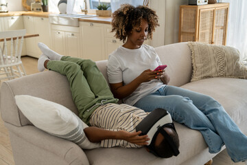 Involved in 3D video game mixed race little boy in virtual glasses lies on couch with concentrated...