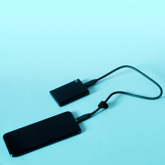 Modern mobile phone and an external portable SSD connected to it on light gradient background. Portable Solid State Drive. OTG interface. Technology, gadgets and the use of SSD disk