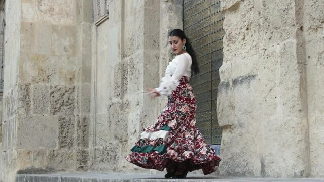 Hispanic gypsy woman flamenco dancer dressed in typical flamenco dress with red flowered skirt and white shirt dancing next to a wall of an old building