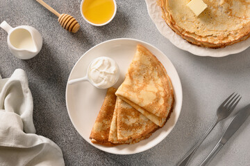 Thin pancakes or russian blini with butter , honey, sour cream on gray stone background. Top view.