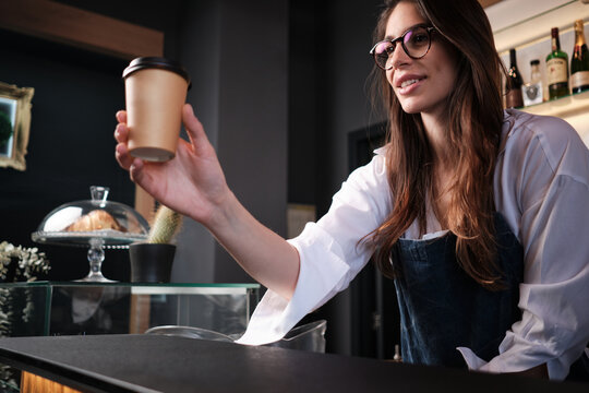 A Friendly Barista Giving Coffee To Go To A Customer While Standing Behind A Bar Counter.