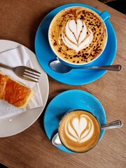 Top view of decorated cups of coffee (coffee art) and slice of lemon drizzle cake