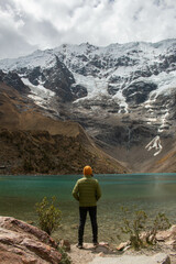 Young man standing on his back in front of the Humantay lagoon in Peru, wearing colourful clothes.