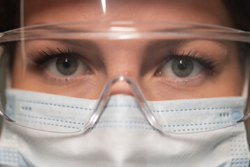 Young woman doctor or nurse working. Girl in medical mask, glasses and shield.