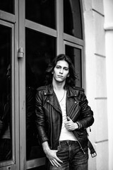 Black and white photo of a young man with long hair.in a leather jacket and jeans